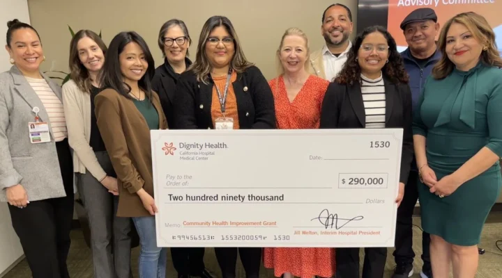 A group of people pose indoors holding a large presentation check for $290,000 from Dignity Health, labeled as a Community Health Improvement Grant.