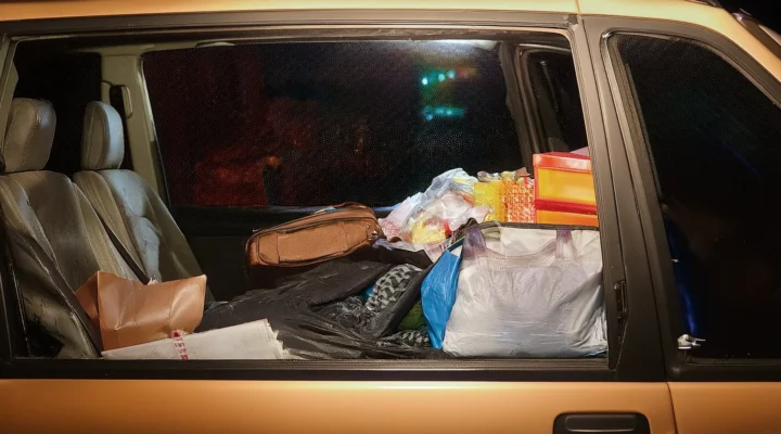 The back seat of a car filled with bags, boxes, and various items, viewed from the side window at night.
